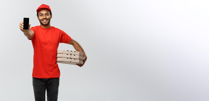 Delivery Concept - Portrait of Handsome African American delivery man or courier with pizza box showing mobile phone on you to check the order. Isolated on Grey studio Background. Copy Space