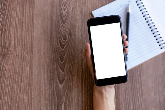 Top view female hands holding smart phone with blank white screen. Women hands workspace, close-up hand holding smartphone blank screen for text and content on wood table background.