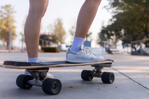Close-up Asian women surf skate or skateboard outdoors on beautiful morning. Happy young women play surf skate at ramp park on morning time. Close up Asian women leg wear sneaker play surf skate 