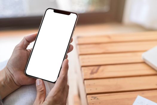 Top view close up female hands holding smart phone with blank white screen. Women hands workspace, close-up hand holding smartphone blank screen for text and content on wood table background.