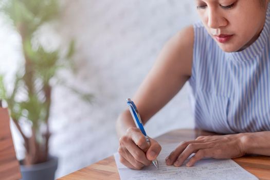Business women use pen writing document paper. Female hand close up writing with a blue pen on a white sheet. Woman writes information on a piece of paper.
