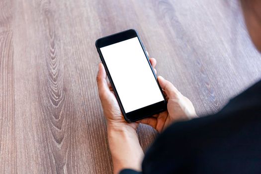 Top view female hands holding smart phone with blank white screen. Women hands workspace, close-up hand holding smartphone blank screen for text and content on wood table background.
