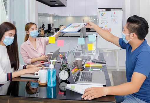 Asian small business start up working with laptop and  PC. Group of asian people teamwork work from Private Home Office social distancing among Coronavirus outbreak Soft focus photo
