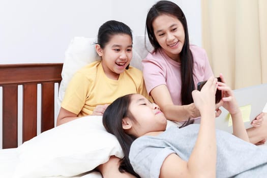 Happy Asian family enjoy and relax on bed in bedroom. mother and daughters enjoy using tablet together on bed.  Family concept.