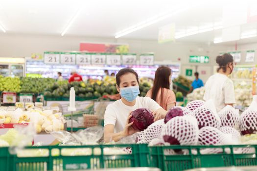 Asian woman long hair wearing protective face mask  in supermarket department store. Female, looking grocery to buy  some fruit. New normal after covid-19. Family concept.