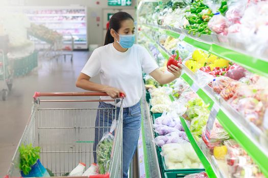 Asian woman wear face mask push shopping cart in supermarket. Girl looking grocery to buy something During coronavirus crisis or covid19 outbreak. Women wearing protective face mask new normal concept