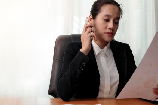 Business women holding smart phone to speak with partners, customers, team and analysis paper chart at office. Business people call for working with customer or partner with smart phone. Business concept.