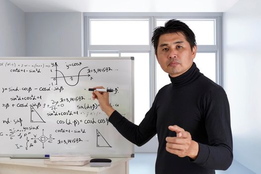 Mature professor teaching mathematics to students in classroom. Teacher man solving math problem while writing on white board with video conference. Covid-19 learn from home.
