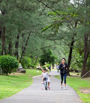 Family in park concept. mother and her daughter play at park together. Mother runing  jogging with daughter samll bike ride. Happy family smiling and enjoy playing at park