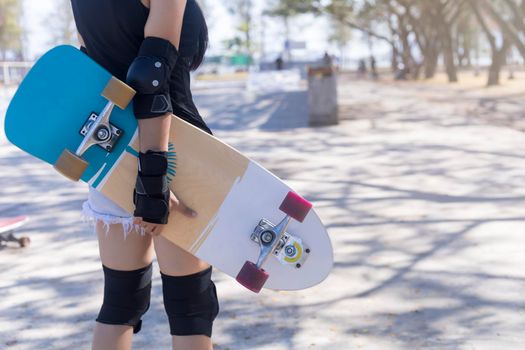 Close up on young women wear protection and hand hold skateboard, surf skate on public skate ramp park background. Free relax skateboard surf skate trendy concept. Fashion portrait of female hands holding surf skateboard