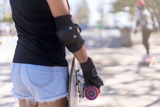 Close up on young women wear protection and hand hold skateboard, surf skate on public skate ramp park background. Free relax skateboard surf skate trendy concept. Fashion portrait of female hands holding surf skateboard
