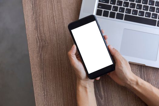 Top view female hands holding smart phone with blank white screen. Women hands workspace, close-up hand holding smartphone blank screen for text and content on wood table background.