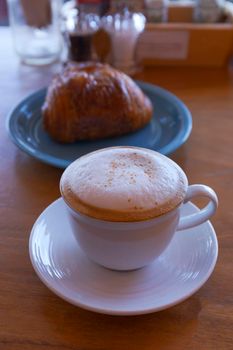 Close up hot cappuccino, latte, caramel macchiato on table with blur coffee shop background. Hot cappuccino coffee on wood table with blur croissant background. breakfast at coffee shop. softfocus select coffee