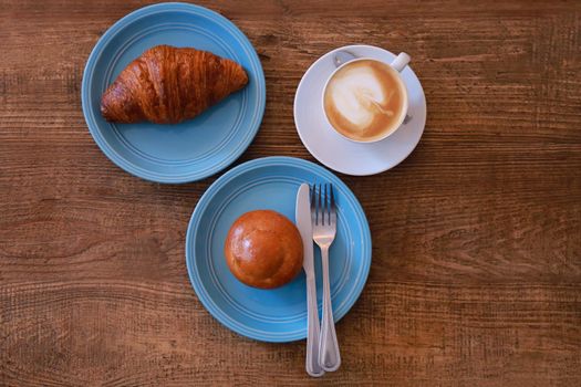 Top view hot cappuccino, latte on wood table with croissant and bun  in coffee shop. Breakfast at coffee shop.