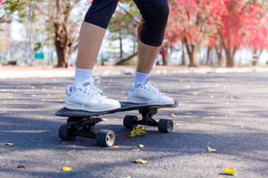 Close-up and motion movement Asian women surf skate or skateboard outdoors on beautiful morning. Happy young women play surf skate at park on morning time. Close up Asian women leg wear sneaker paly surf skate on public park. Sport concept