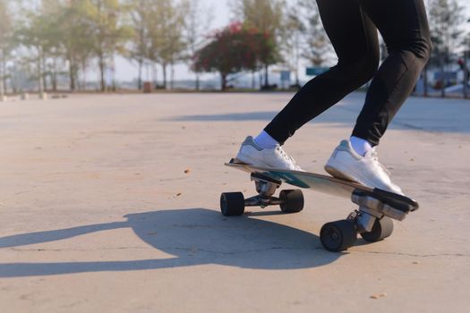 Close-up and motion movement Asian women surf skate or skateboard outdoors on beautiful morning. Happy young women play surf skate at park on morning time. Close up Asian women leg wear sneaker paly surf skate on public park. Sport concept