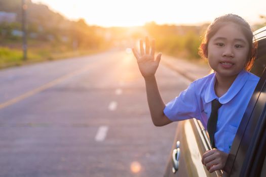 On the way to school, the little girl stretched out his hand from the car window, laughing and smiling. Asian little girl smiling  and waving hand out the car. Children relax with street view from the car. Family in car concept.