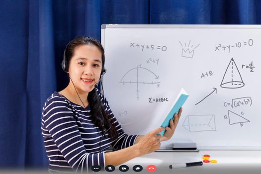 Asian school woman teacher working from home teach online math to student studying from home. Teacher writeing on whiteboard and talk on headset internet education class during covid19 pandemic
