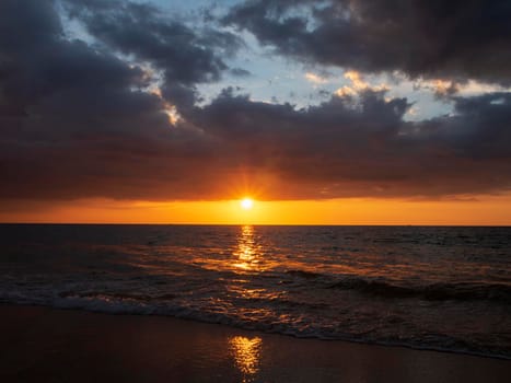 Beautiful sunset over the calm sea with cloud sky background. Sunset over tropical beach. Nature summer  concept. Peak sunset over sea with yellow light reflect on sea water. Tranquil seascape. 