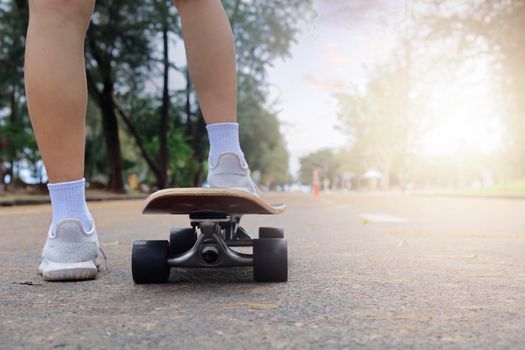 Close up rear view Asian women leg on surf skate or skate board in outdoor Park. Closeup leg wear white sneakers put on surfskate at public park. Extreme sport and relax concept