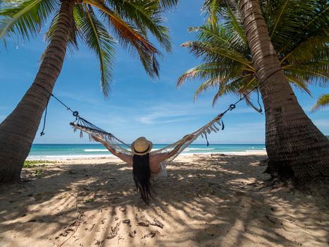 Phuket Thailand. Asian young woman relaxing on hammock by the beach at sunset. Young attractive female swinging on hammock. Holiday vacation summer