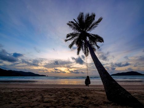 Phuket, Thailand. Tropical beach paradise with beach swing with women sitting. sunset with silhouette women relax on swing under coconut palm tree at beautiful tropical beach vacation summer holiday concept