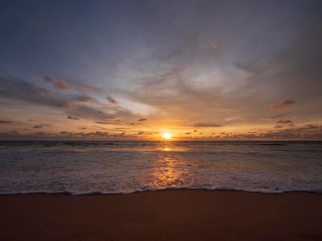 Beautiful sunset over the calm sea with cloud sky background. Sunset over tropical beach. Nature summer  concept. Peak sunset over sea with yellow light reflect on sea water. Tranquil seascape. 