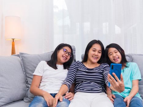 Happy family sitting on sofa in living room speak with someone on mobile phone together, smiling mother showing cute little child video call by smartphone speak with family.