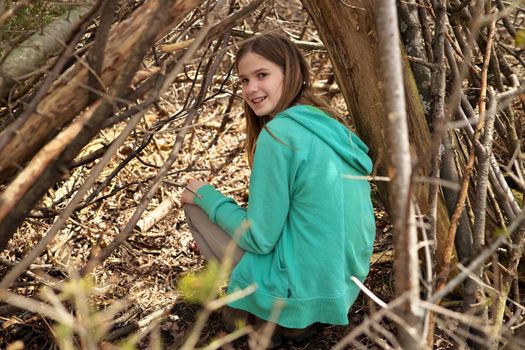 Young adolescent girl outside in the forest with lean-to tree fort treehouse tree house hangout she built. High quality photo