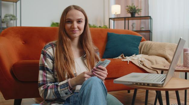 Planning family budget. Smiling happy young woman counting money cash, use laptop computer calculate domestic bills at home. Joyful girl satisfied of income and saves money for planned vacation, gifts