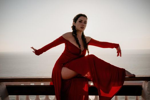 Closeup video portrait of sensual young brunette woman in red dress, happily dancing outdoors isolated on blurry sea background with natural bokeh in soft warm sunset backlight