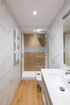 Shower zone with wooden finishing and glass door. Interior of modern refurbished bathroom.