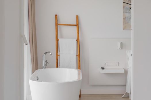 White empty bathtube in interior of modern stylish hotel bedroom connected wit bathroom. Metal faucet and white towels on a decorative wooden staircase