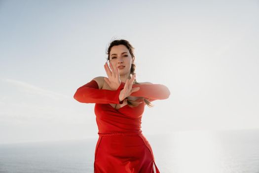 Closeup video portrait of sensual young brunette woman in red dress, happily dancing outdoors isolated on blurry sea background with natural bokeh in soft warm sunset backlight