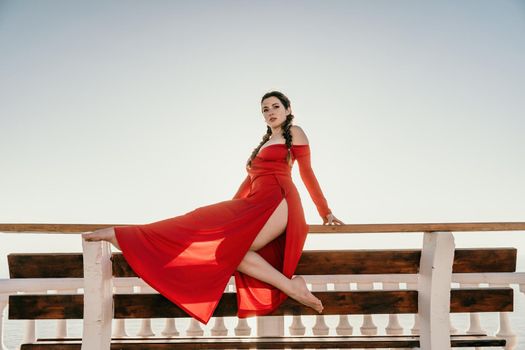 Closeup video portrait of sensual young brunette woman in red dress, happily dancing outdoors isolated on blurry sea background with natural bokeh in soft warm sunset backlight