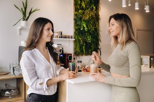 Two sporty-looking girls with cocktails in their hands discuss healthy eating and diet.