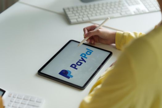 CHIANG MAI, THAILAND - MAY 11 2022 : Woman using Ipad with paypal logo on screen. PayPal is a worldwide online payment system and one of the most popular ways of making payment on the Internet