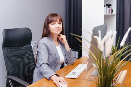 A brunette woman at a computer in the workplace. Business concept.