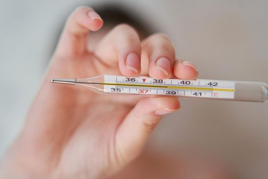 Girl holds a thermometer. High body temperature on a thermometer. Close-up.