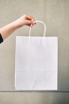 Young woman holding white paper disposable bag in hand on gray background.