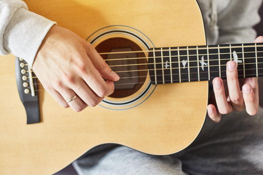 Cropped shot of man practicing in playing acoustic guitar. Close-up of man hand playing guitar.