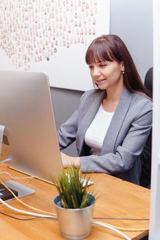 A brunette woman at a computer in the workplace. Business concept.