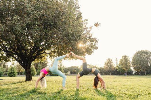 Sport gymnastics excercises of 2 girls outdoor in the green park. Gymnastics support exercise