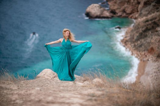 A woman in an emerald dress, a fashion model with long silk wings in a flowing dress, flying fabric on the embankment
