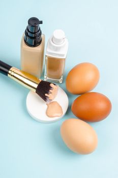 The Liquid fluid foundation glass bottle on makeup sponges and egg on blue background. Choose tone color foundation makeup for skin concept.