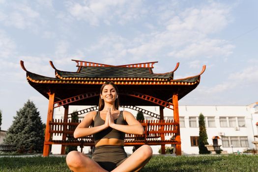 Praying and meditation in lotus position. Fit girl is sitting and meditating outdoors near chinese gazebo