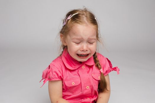 Little girl in pink shirt looking aside and crying on isolated background. Scared sad child screaming in studio. Unhappy kid weeping. Concept of violence, offense and childhood.