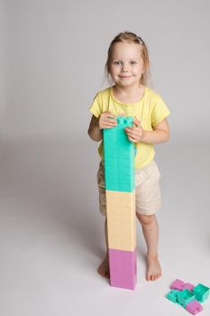 Stock photo portrait of lovely little girl holding high colored blocks constructed by herself. Cute smiling girl playing with plastic colorful blocks in studio. She is smiling at camera happily.