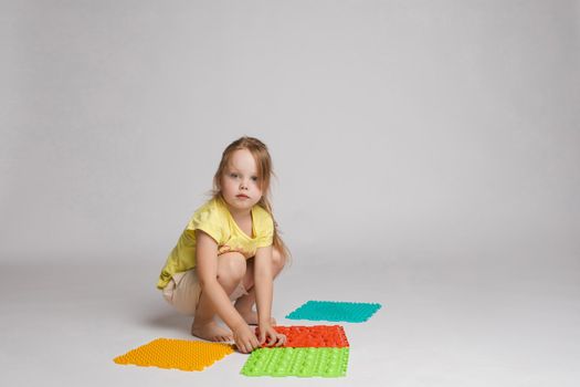 Stock photo of a child playing with colorful bright rubber pads for improving and developing fine motor skills on the floor. She is sitting on her haunches in studio.