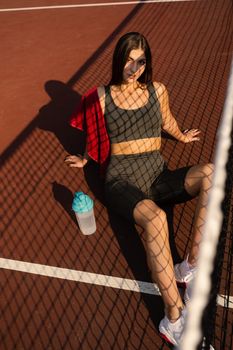 Sport lifestyle. Sport girl with bottle of water and towel. Asian model sitting on the tennis court